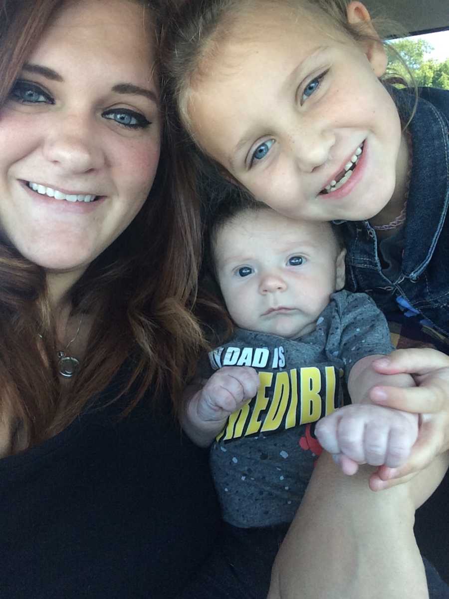 Woman smiles in selfie in car with toddler daughter and baby son