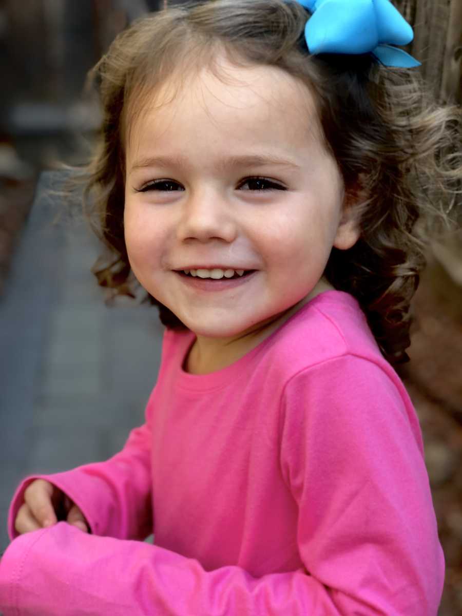 Little girl wearing pink long sleeve with blue bow in her hair smiles