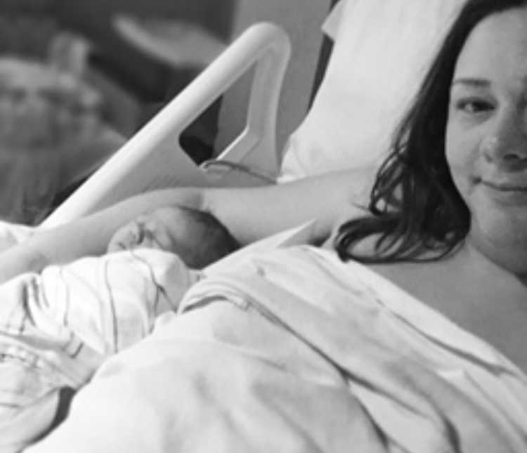 Mother lays in hospital bed with her arm around newborn who is asleep beside her