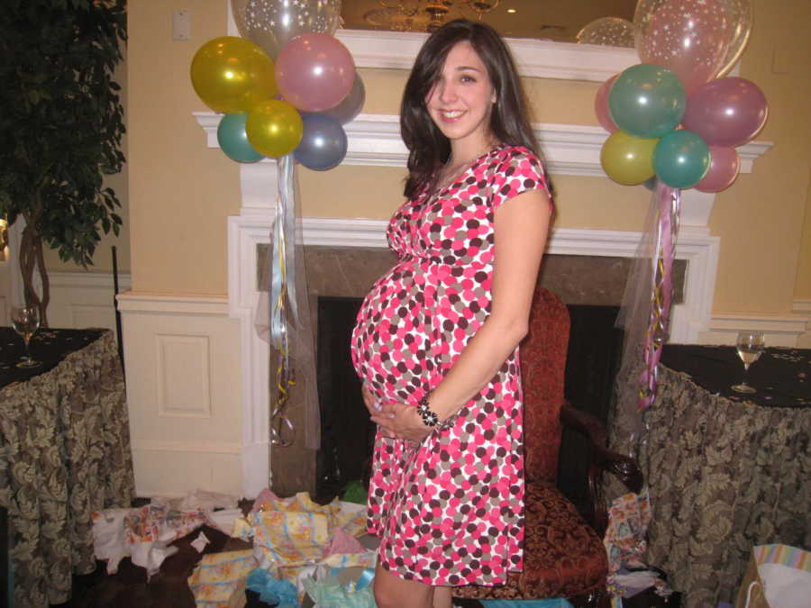 Woman who got pregnant through IVF stands in front of fireplace smiling while holding her stomach