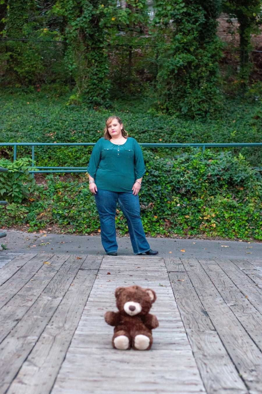 Woman who miscarried stands outside with teddy bear sitting in front of her