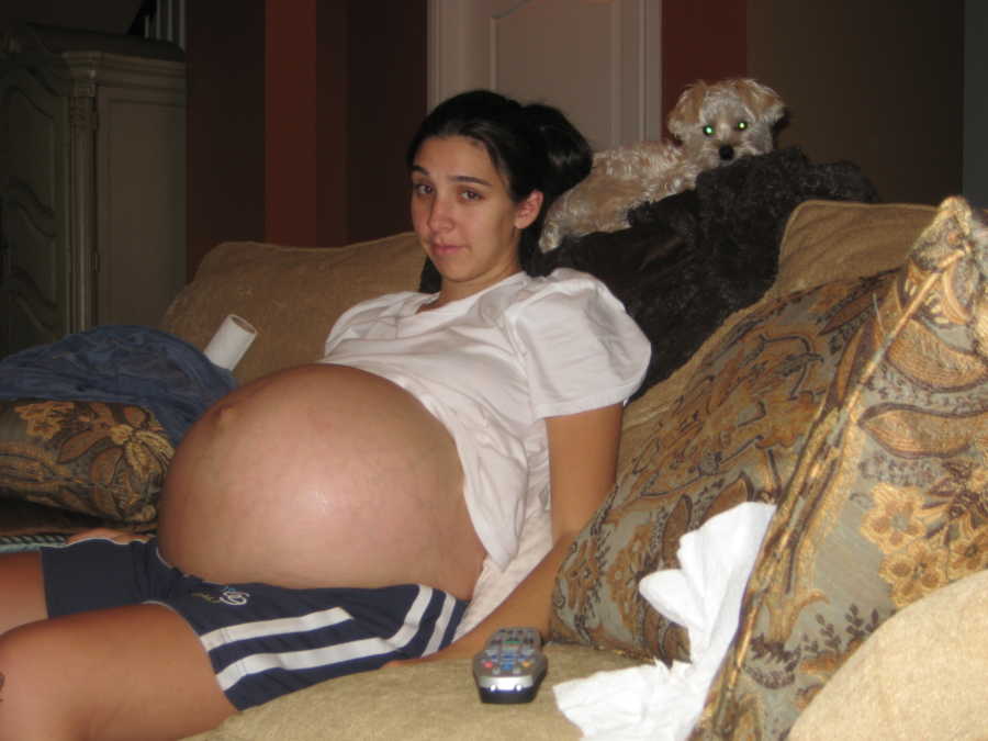 Woman pregnant with triplets via IVF sits on couch with her shirt up exposing her stomach