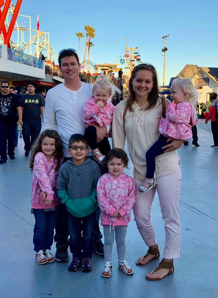 Mother and father stand smiling with their five children at amusement park