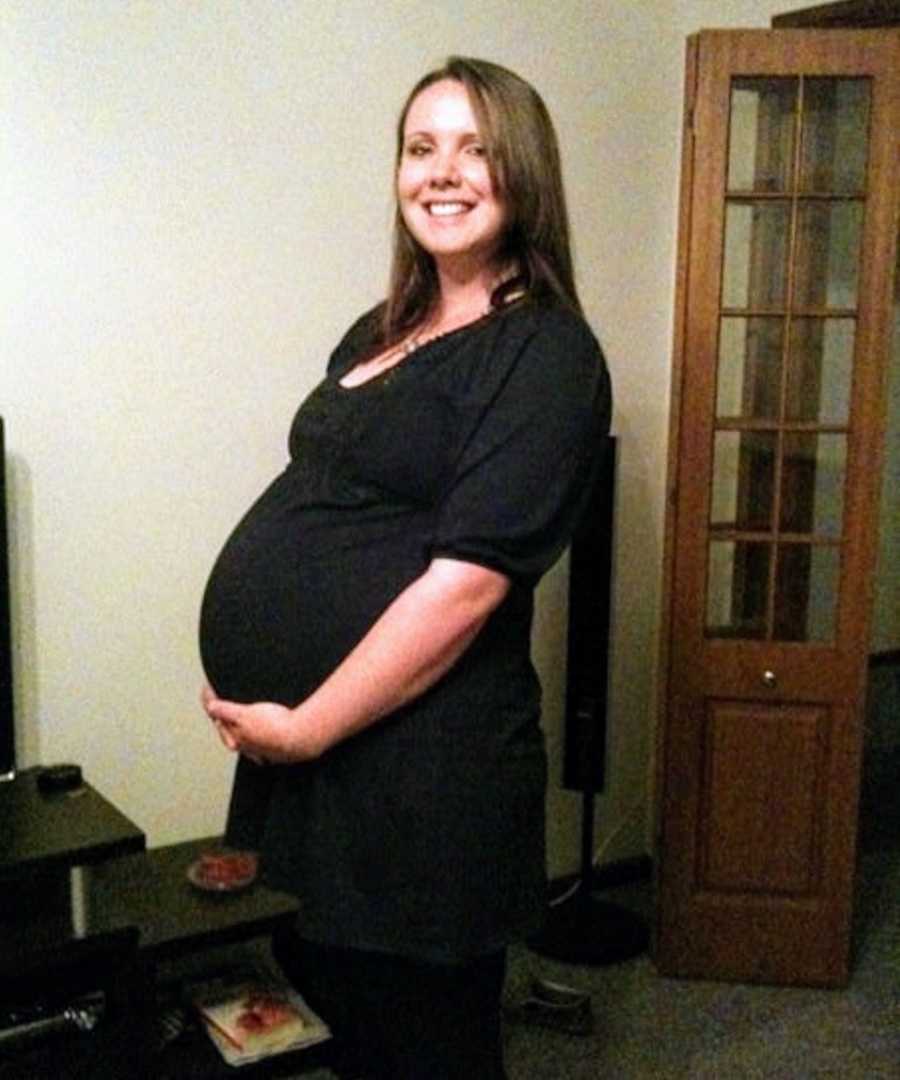 Pregnant woman with Pulmonary Emboli stands smiling while holding her stomach