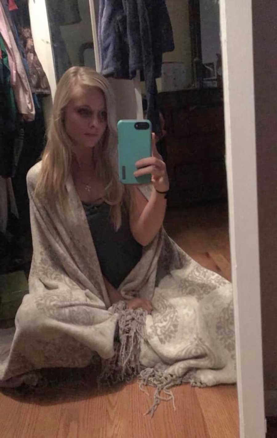 Woman who experienced emotional abused in relationship sits on floor wrapped in blanket taking mirror selfie
