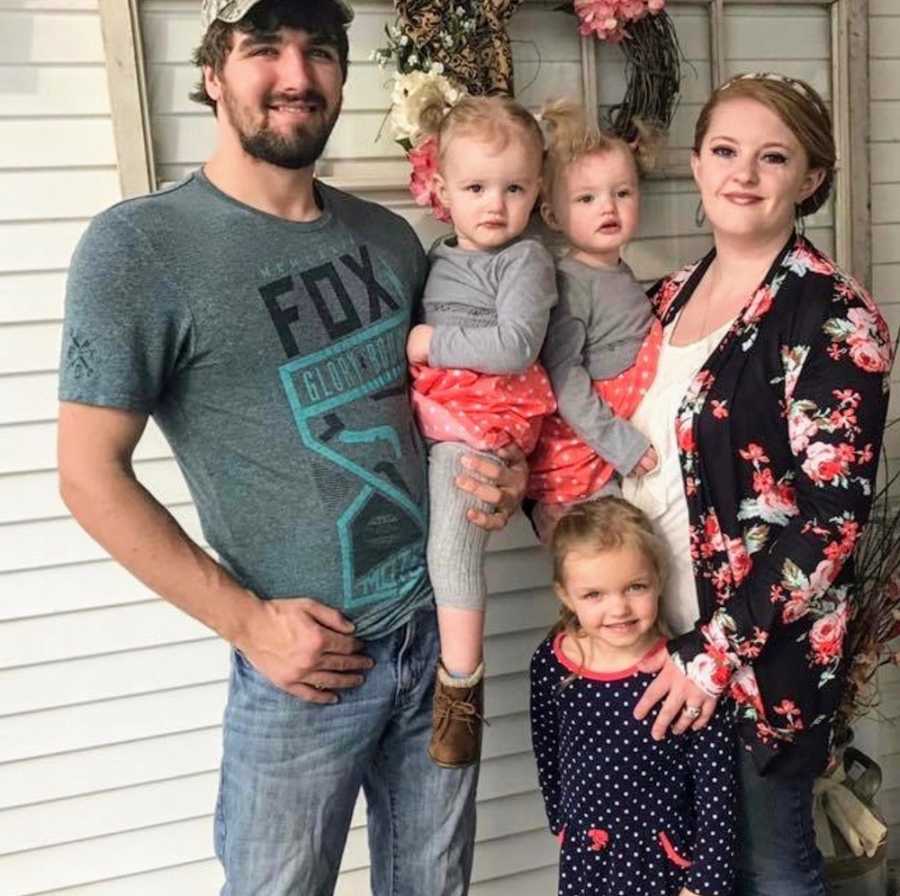 Husband and wife stand holding two of their young girl's while their oldest stands in front of them