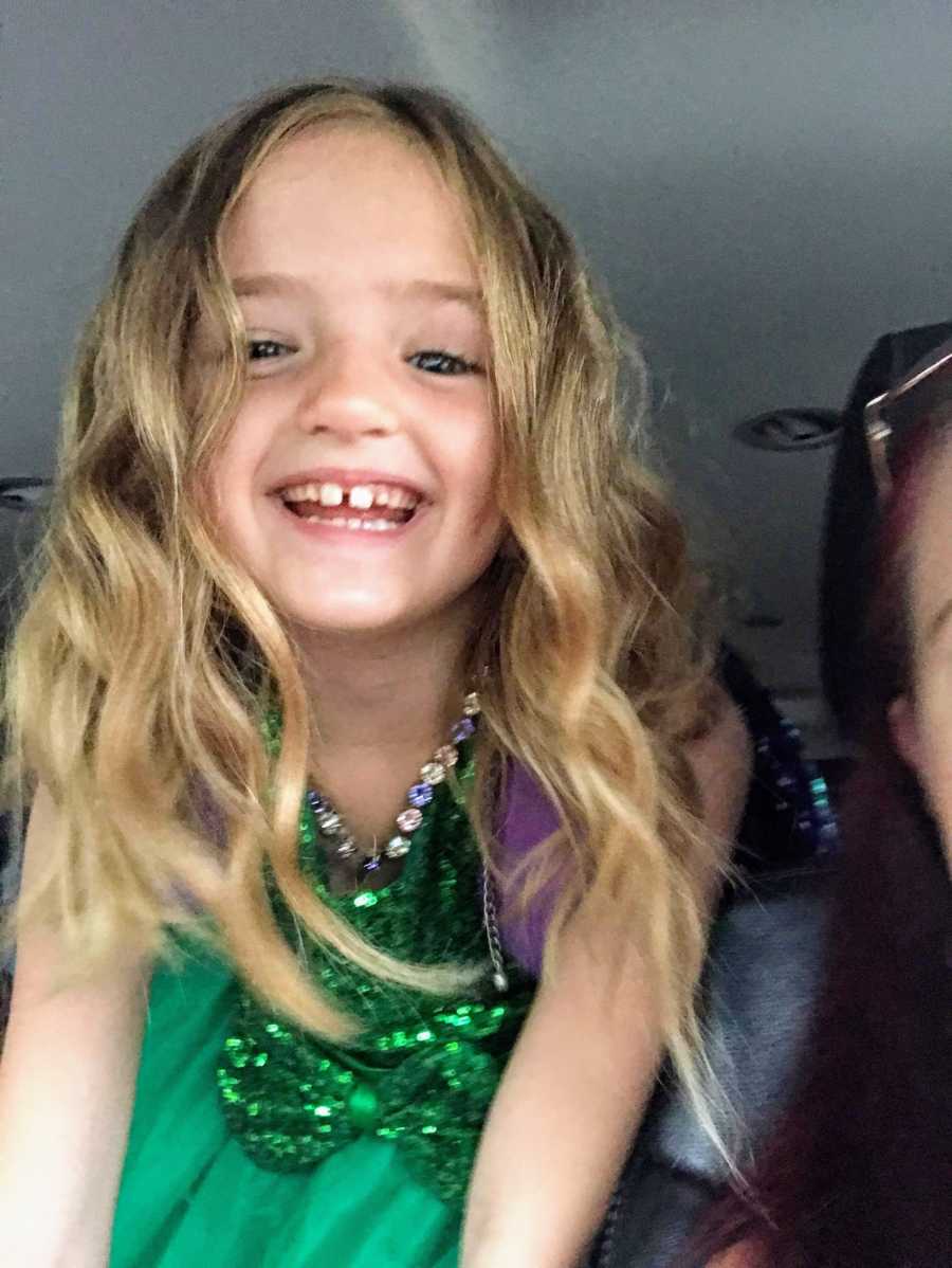 Little girl smiling in car wearing sparkly green dress on picture day