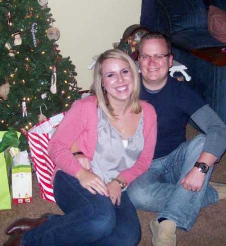 Woman smiles as she sits beside boyfriend on ground next to Christmas tree and presents
