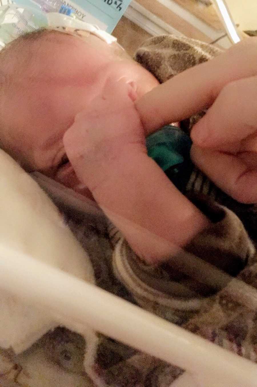 Newborn lying in NICU holding onto mother's finger