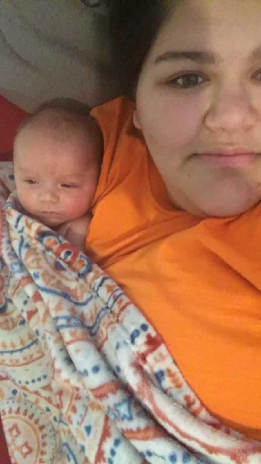 Mother who had postpartum depression smiles in selfie with newborn laying in her arm