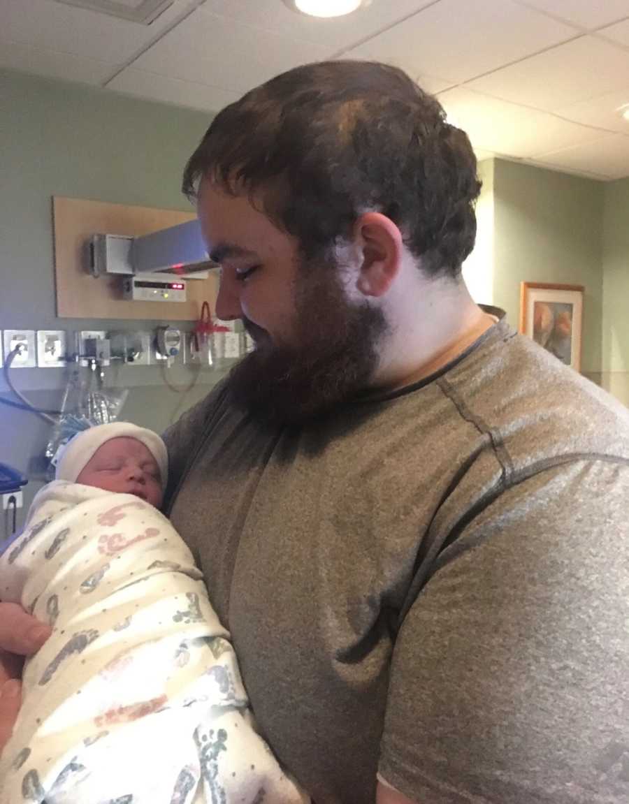 Father holds newborn swaddled in blanket in his arm that has been in NICU