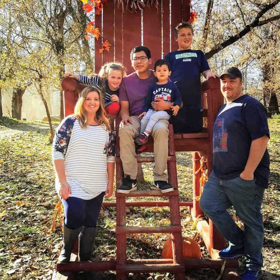Husband and wife stand beside large red chair where two adopted kids and biological kids sit