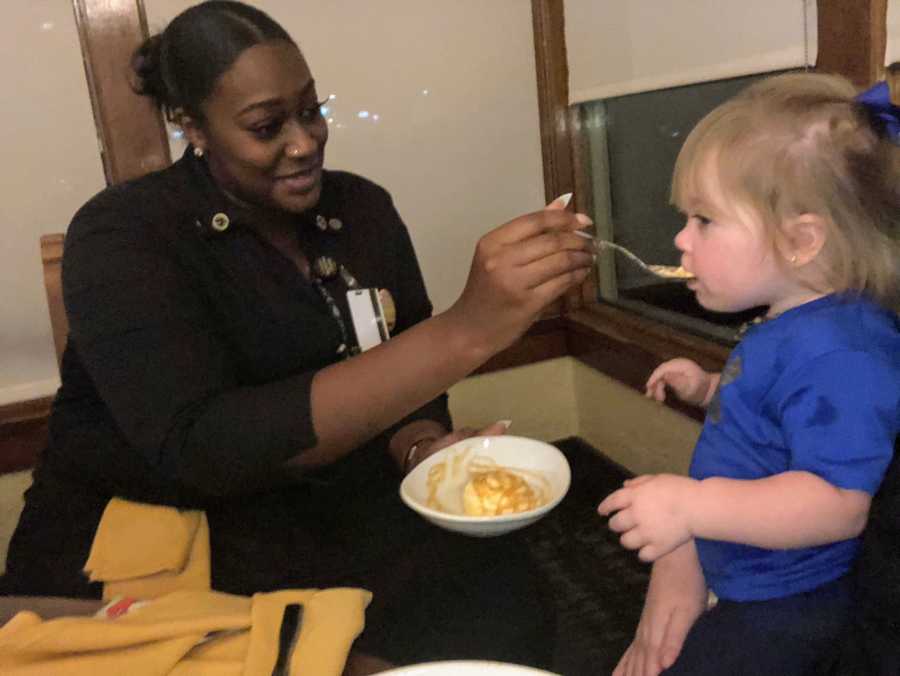 Olive Garden waitress sits at table feeding toddler food