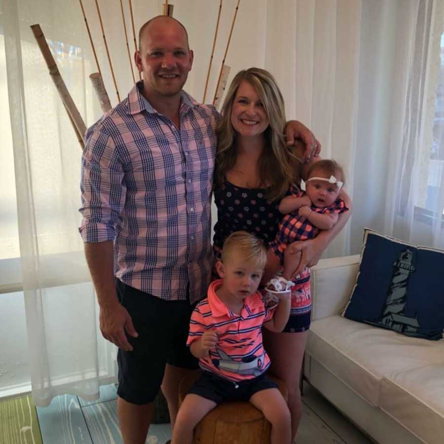 Husband and wife stand smiling with their baby daughter and toddler son 