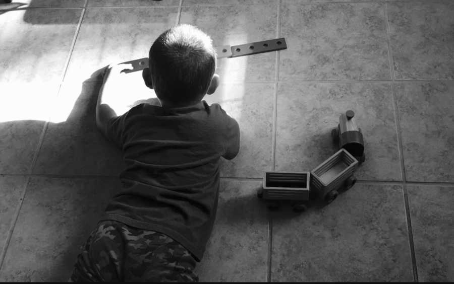 Little boy laying on kitchen floor playing with toys whose little sisters have both passed away