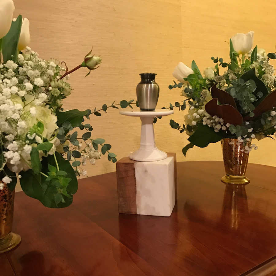 Urn of miscarried baby on podium beside vases of flowers 