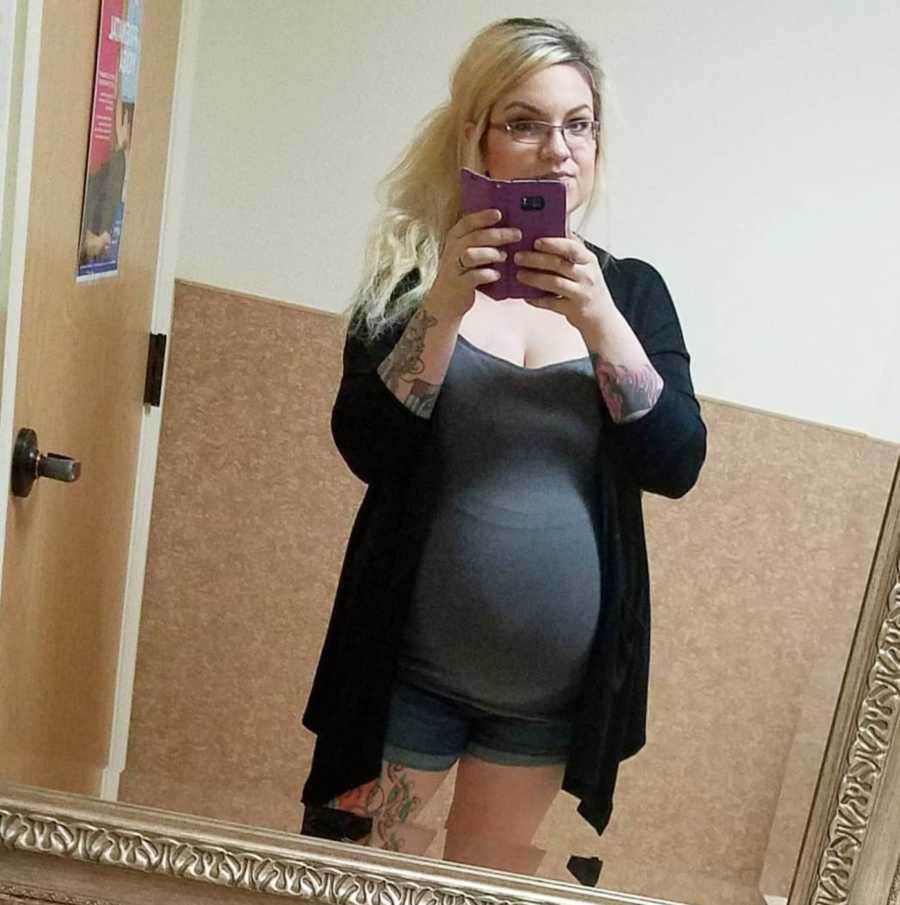 Pregnant woman smiles in mirror selfie in bathroom