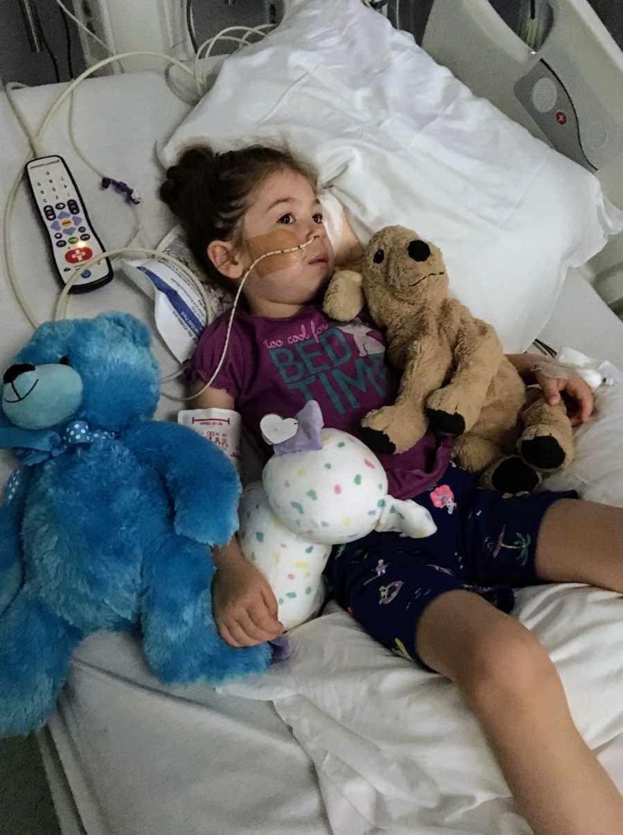 Young girl with polio-like symptoms lays in hospital bed with stuffed animals