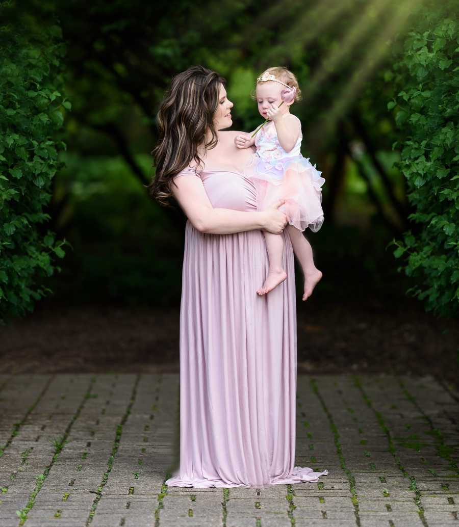 Mother stands in long gown outside holding daughter 