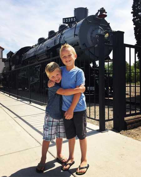 Young boys hugging in front of train whose mother was bullied in school
