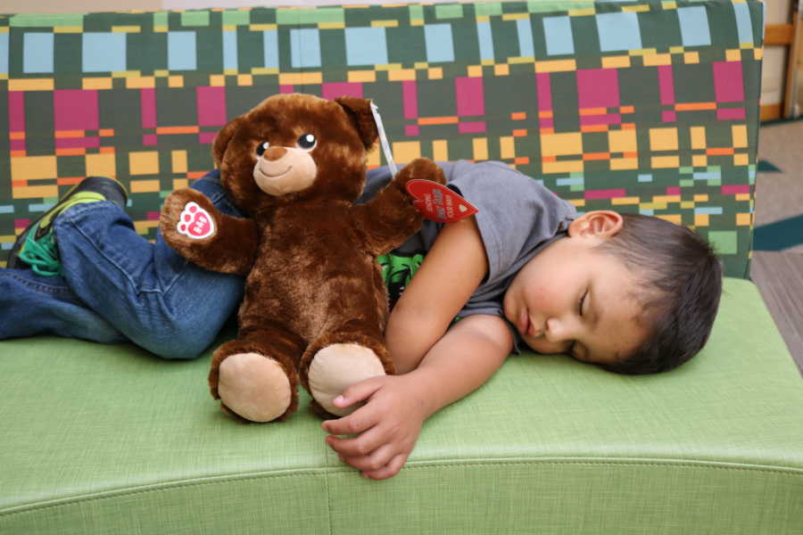 Young boy born without a right arm lays on couch asleep with teddy bear