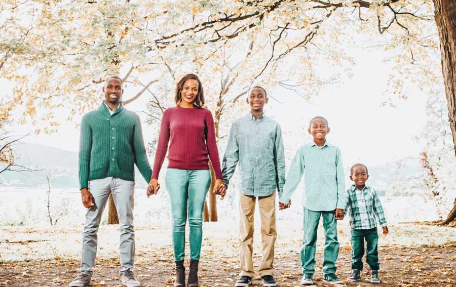 African American family of five hold hands for photoshoot in wooded area