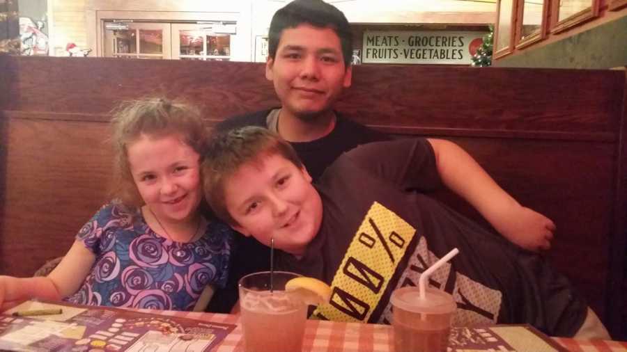 Teen sits in booth of restaurant with foster parent's biological children