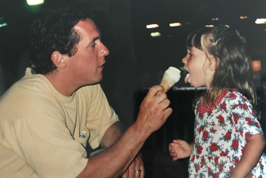 Father holds out ice cream cone for young daughter to lick
