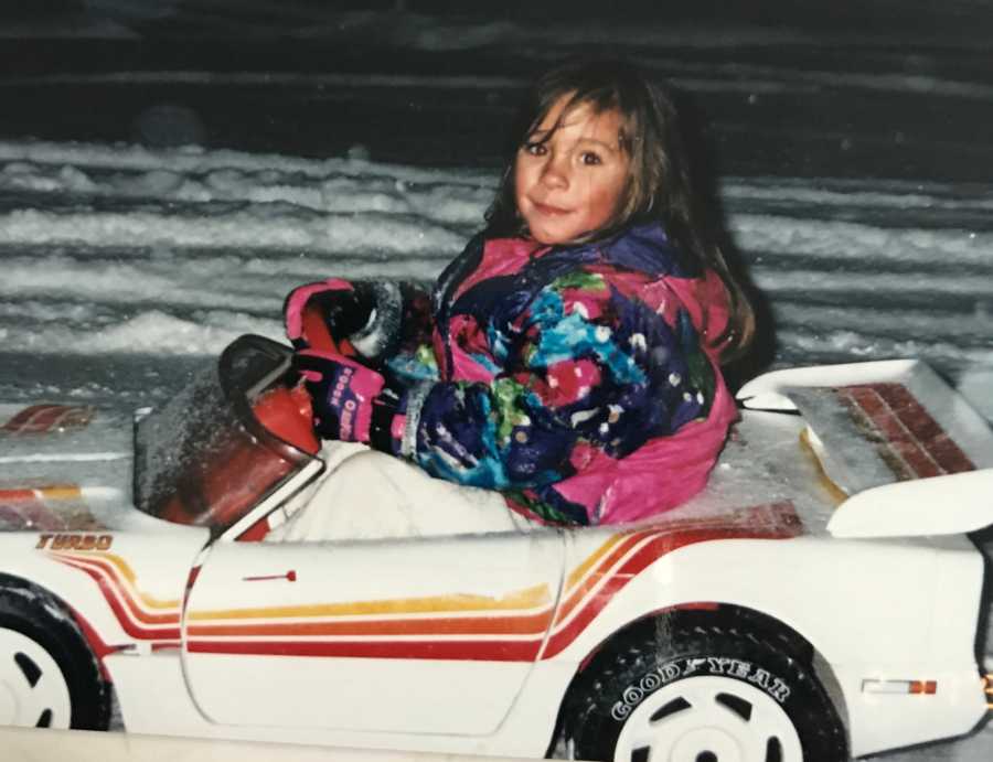 Little girl sitting in electric toy car wearing snow suit