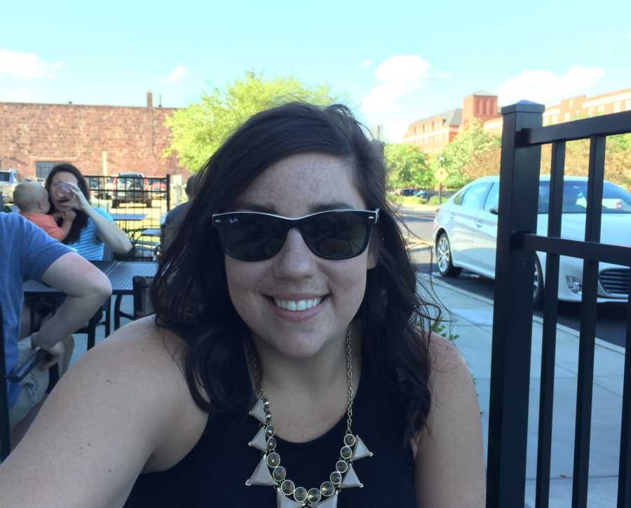 Woman smiles in selfie as she sits at outdoor table of restaurant