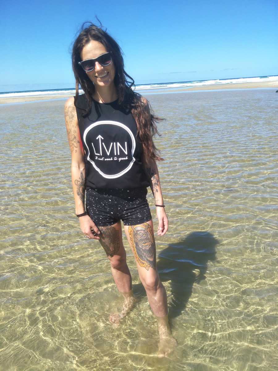 Woman who is recovering from multiple mental health issues stands smiling in shallow ocean water