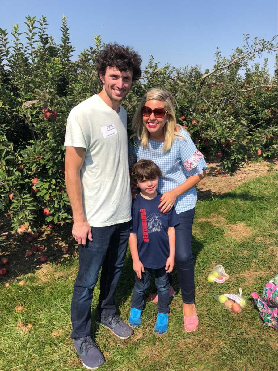 Husband and wife stand with son at apple orchard