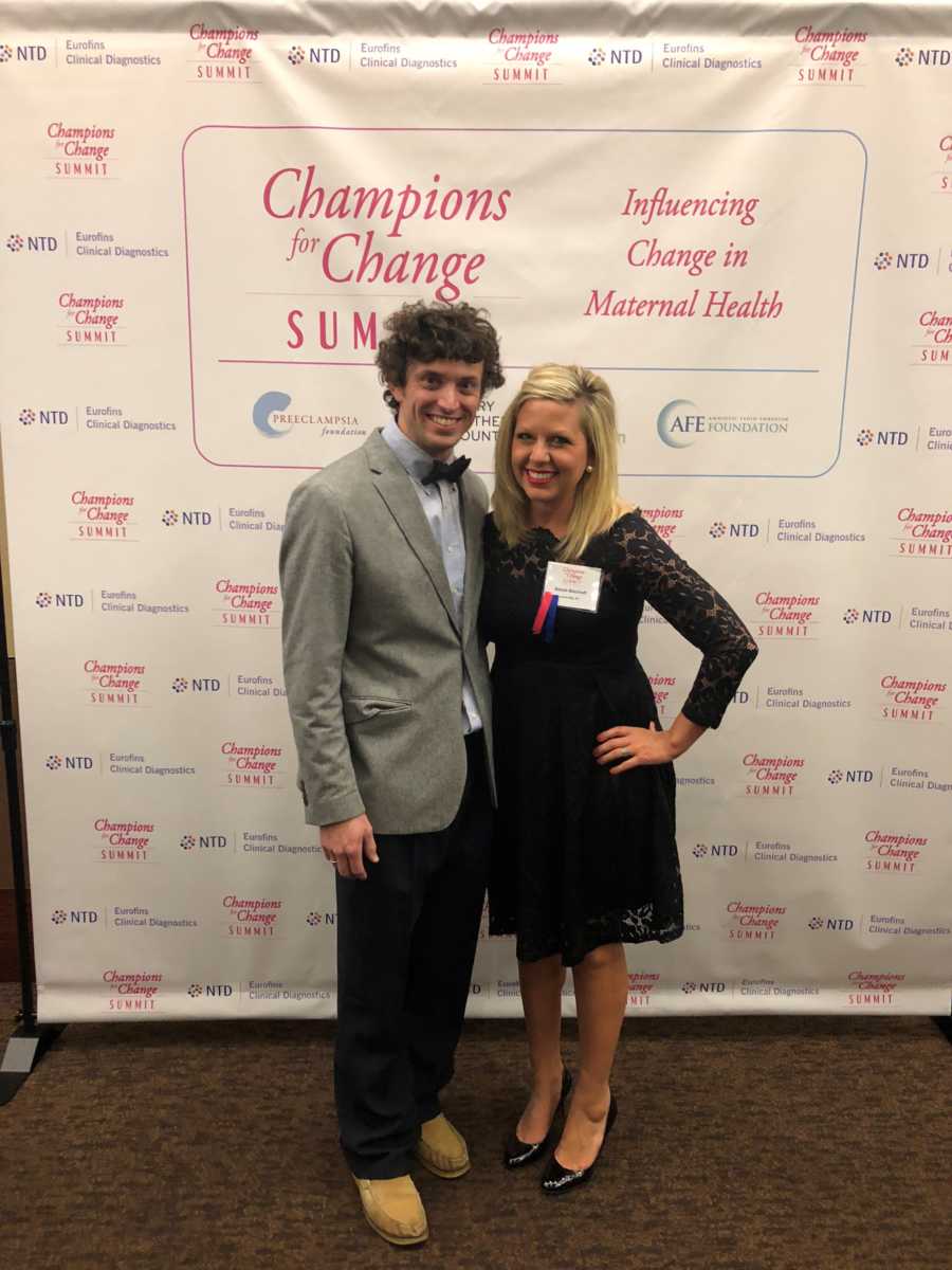 Woman who almost died in child birth stands beside husband in front of backdrop that says, "Influencing change in maternal health"