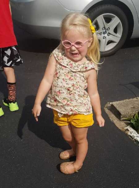 Little girl with pink glasses stands in parking lot with silly face