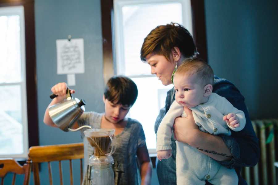 Woman holds foster baby as she watched other foster child make coffee