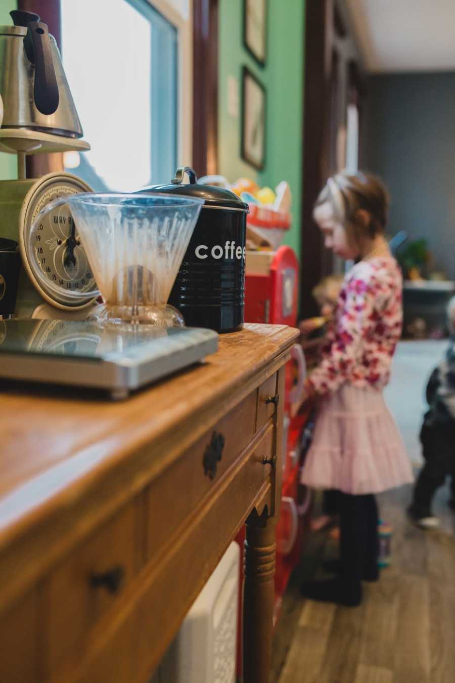 Close up of coffee machine with foster child playing at toy kitchen in background