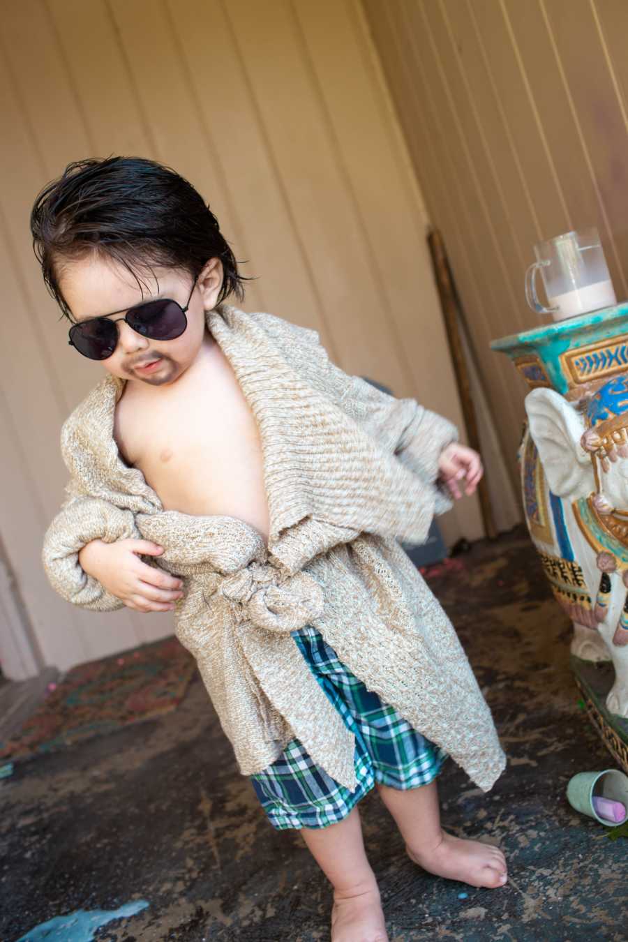 Toddler stands outside wearing robe and sunglasses with drawn on gotee