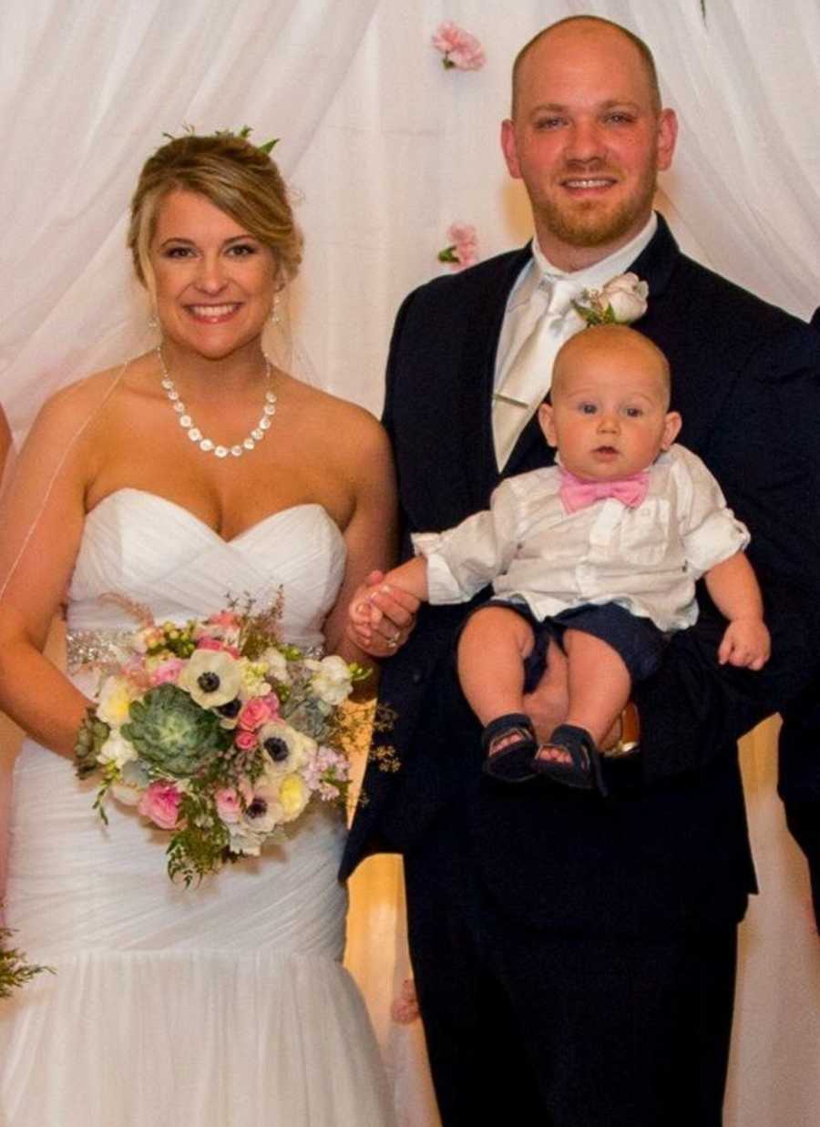 Bride and groom standing with their infant son at wedding