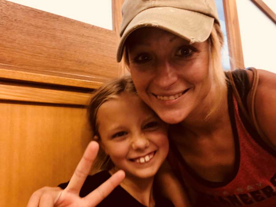 Mother smiles in selfie with her daughter who holds up peace sign who is her best friend