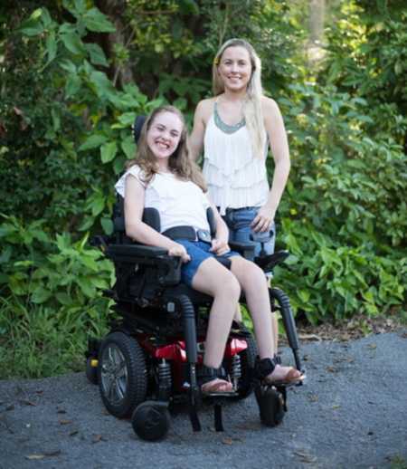 Mother smiles beside daughter who is in electric wheelchair 