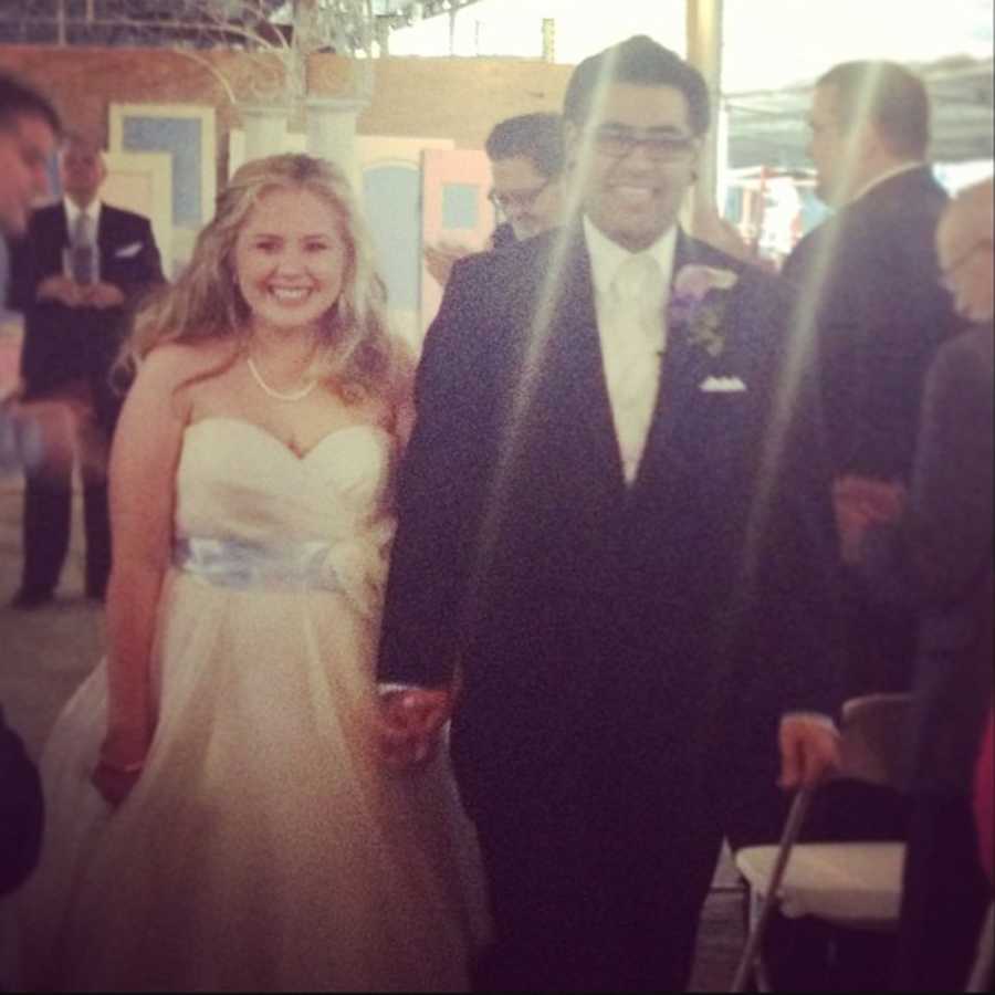 Bride and groom walk down aisle of outdoor wedding smiling and holding hands