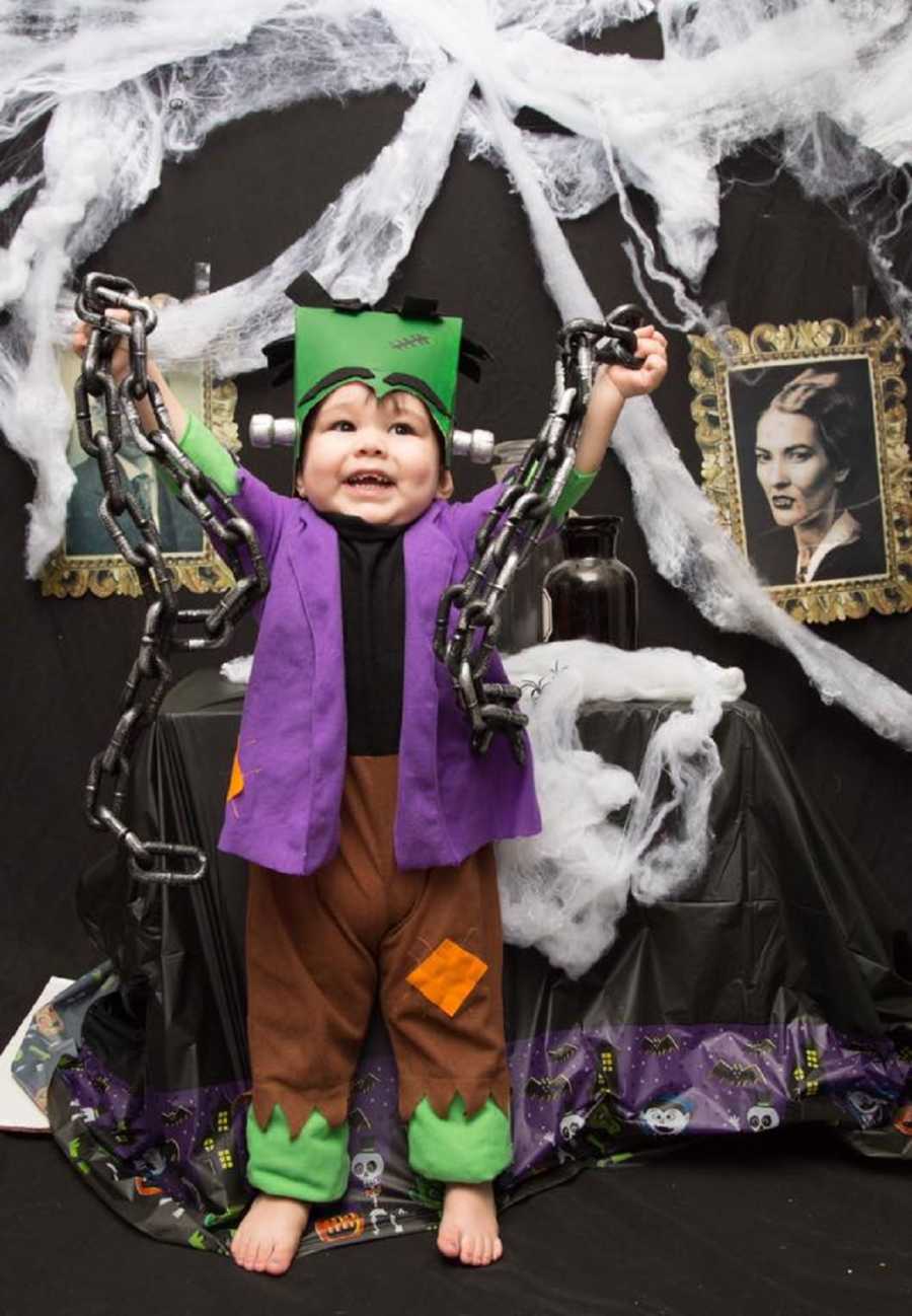 Toddler dressed as Frankenstein smiling with arms in the air