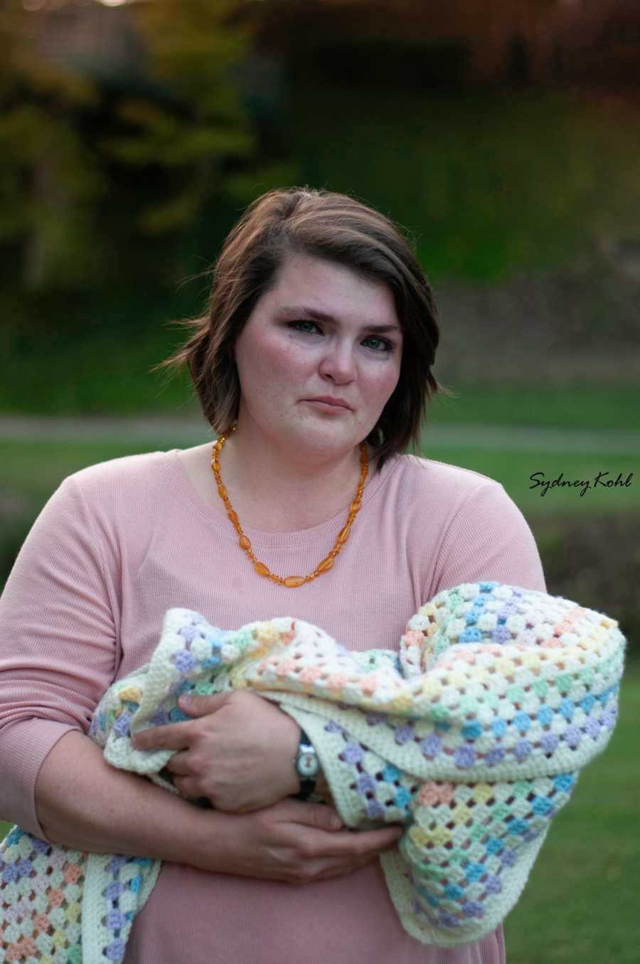 Mother who experienced child loss cries as she holds empty blanket as if there were a baby in it