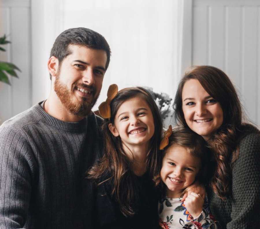 Husband and wife who lose their child sit smiling with other two daughters