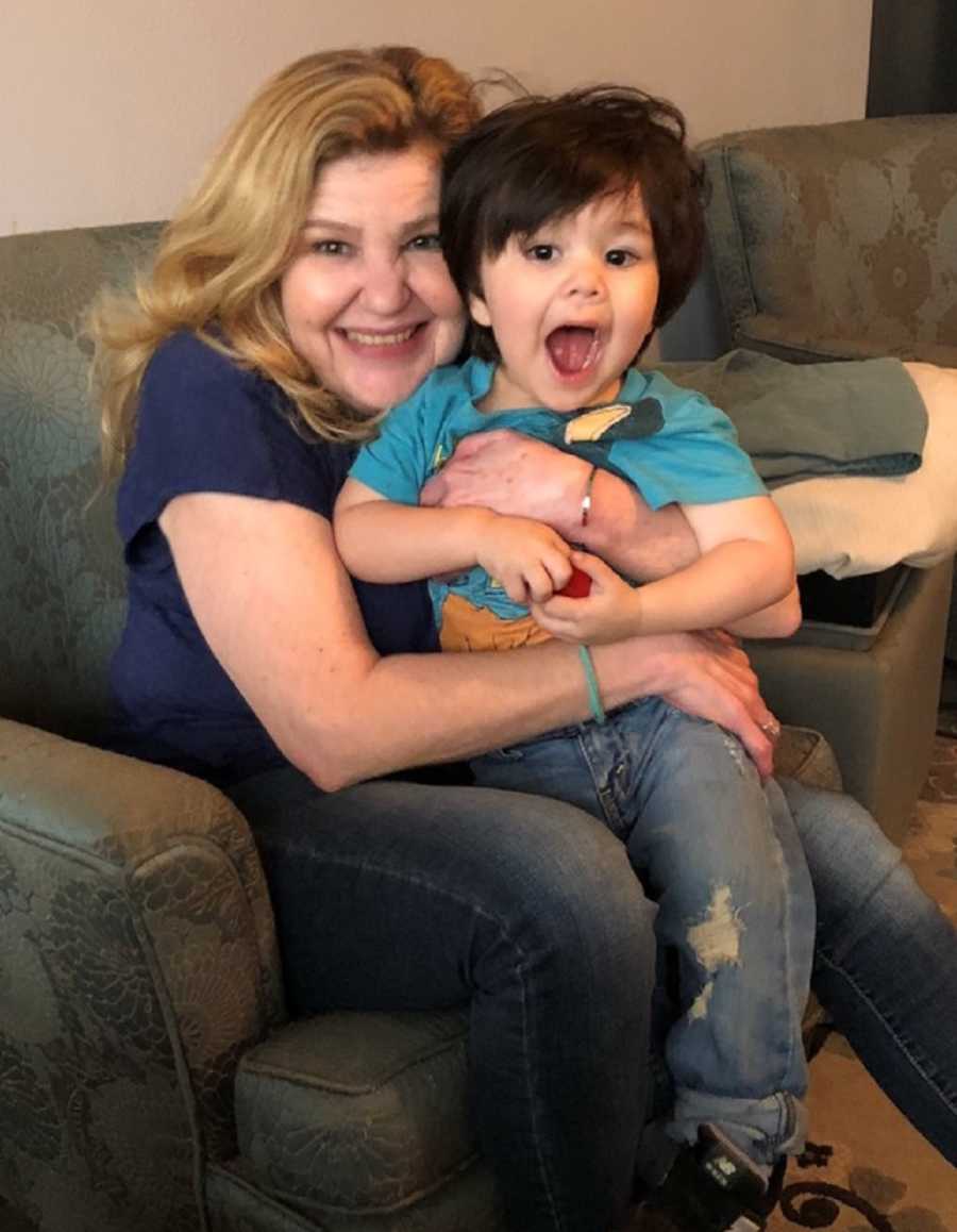 Grandmother sits on chair smiling with grandson sitting in her lap