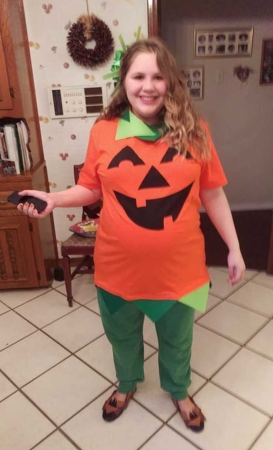 Woman stands smiling in kitchen wearing jack-o-lantern costume
