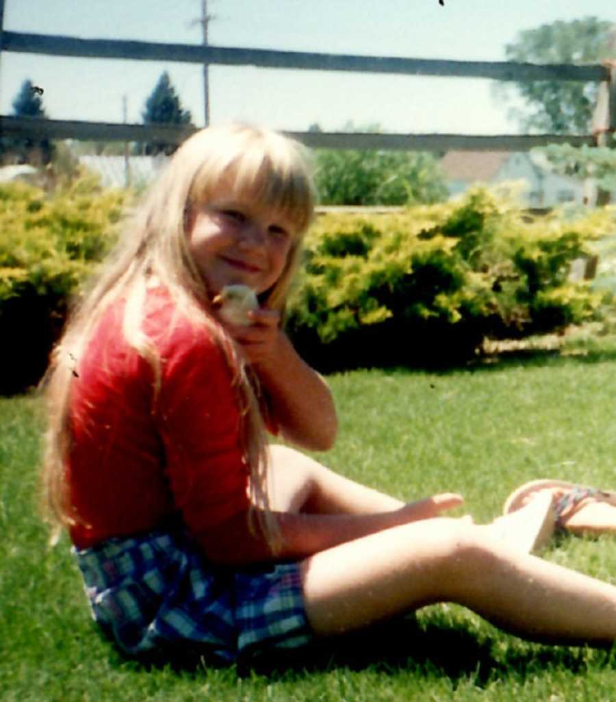 Little girls sits in grass holding a baby duck