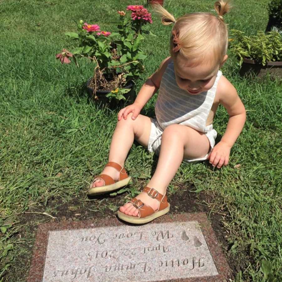 Little girl sitting in grass beside younger sister's grave