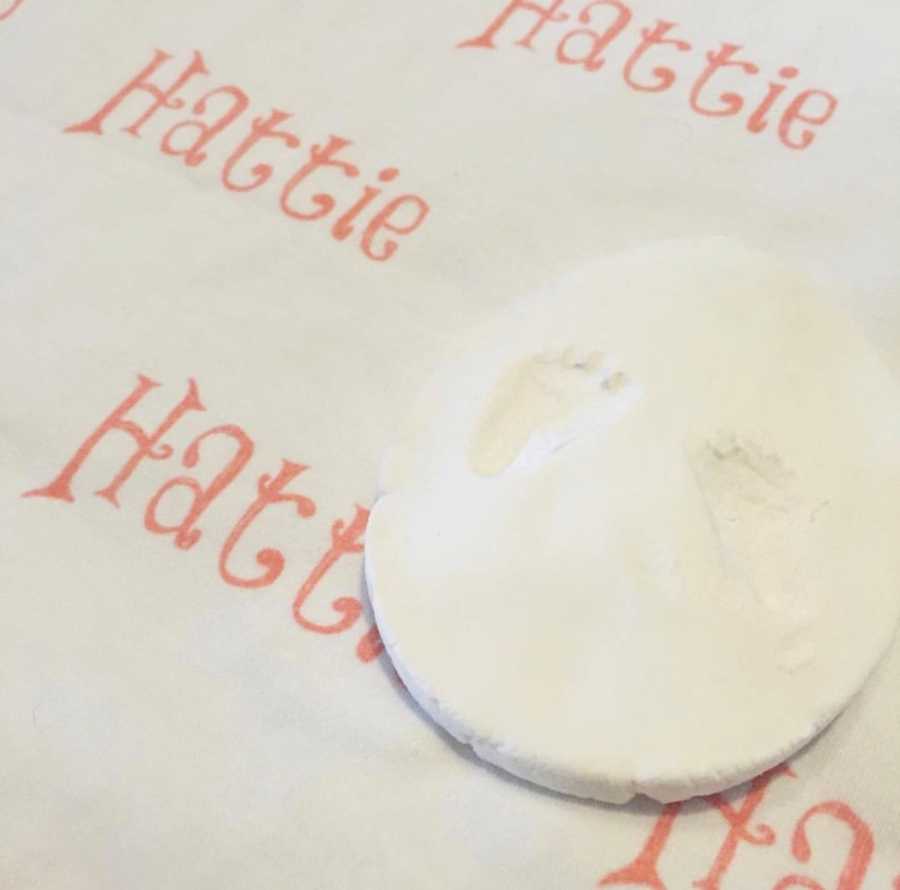 Mold of baby's footprint beside name "Hattie" written in orange beside it