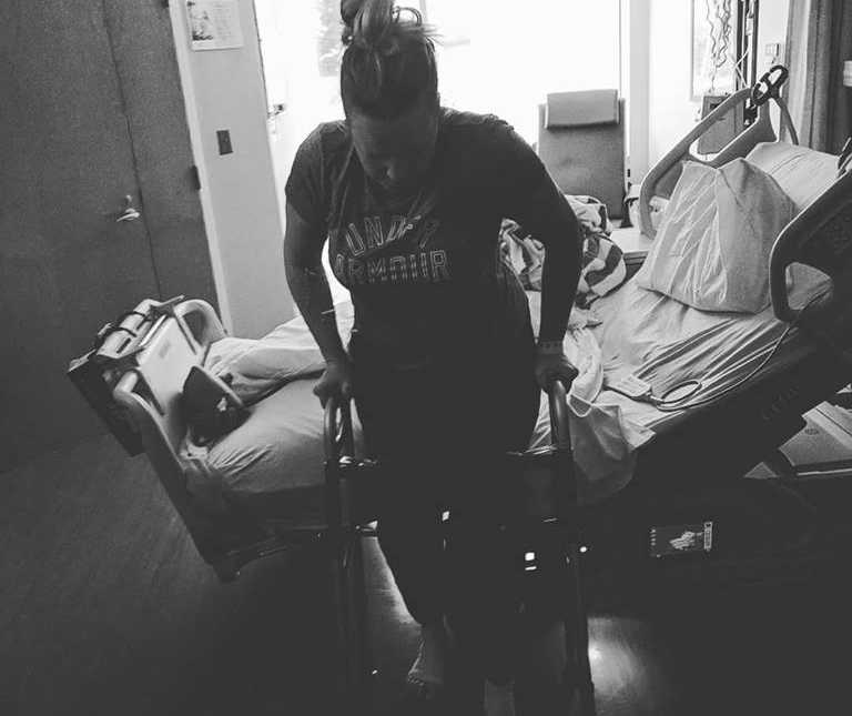 Woman with cancer leans on walker beside hospital bed